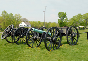 Historic cannons with a grassy field and old house in the background.