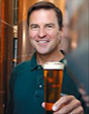 Smiling man holding out a glass of beer to the viewer.